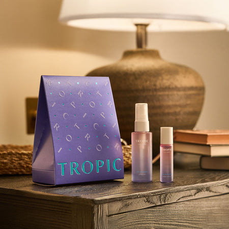 The Pillow Service Aromatherapy Sleep Collection by Tropic displayed on a bedside table, including a purple gift box, a pillow mist spray, and a rollerball, all designed to help promote relaxation and restful sleep.